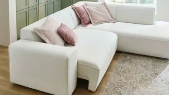 Großzügige Wohnlandschaft in hellen Farben mit roséfarbenen Zierkissen und grün getäfelter Wand – gemütliches, modernes Wohnzimmer mit stilvollem Teppich und Eichenholzboden